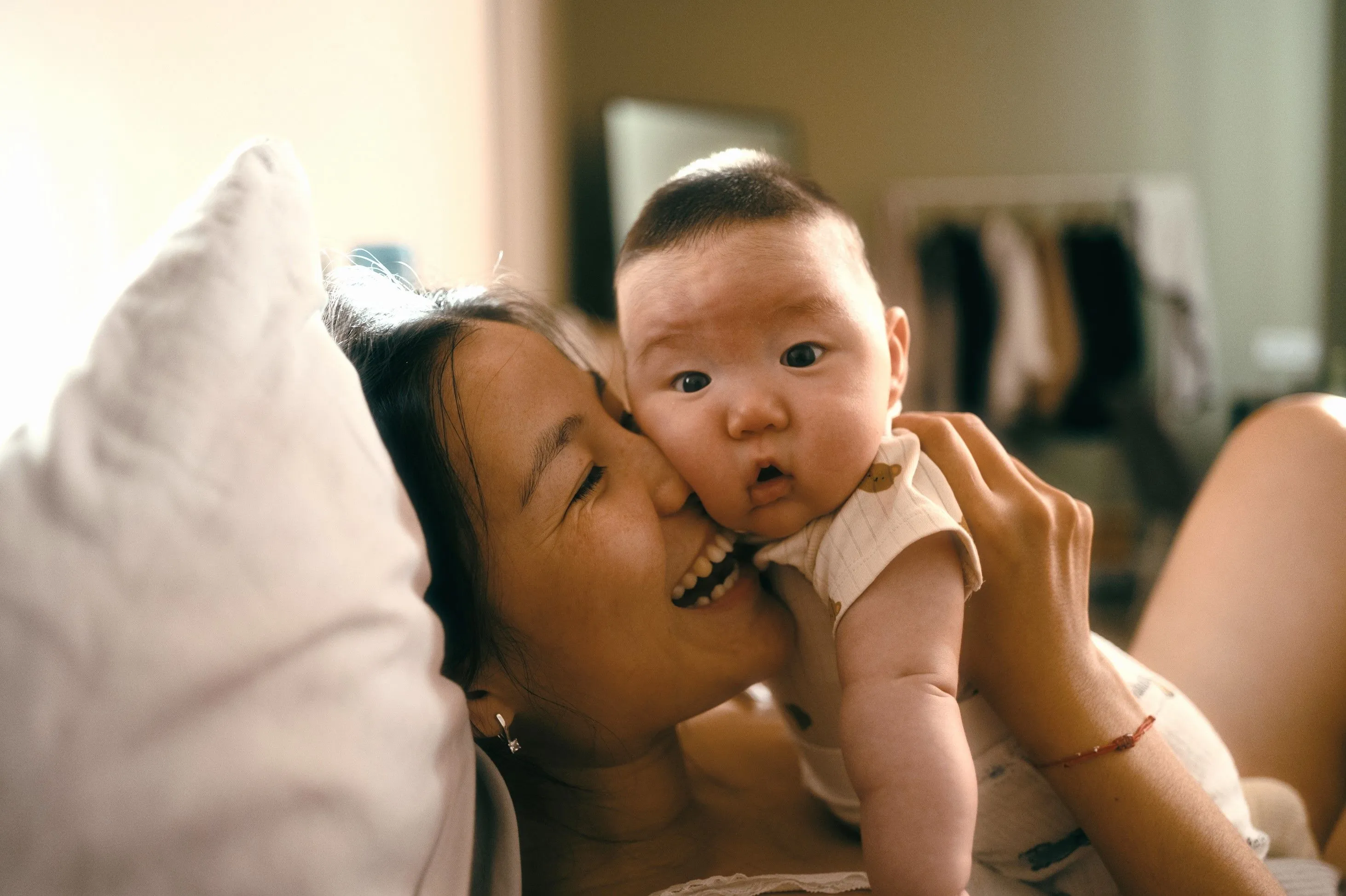 Mother smiling while snuggling baby in bed