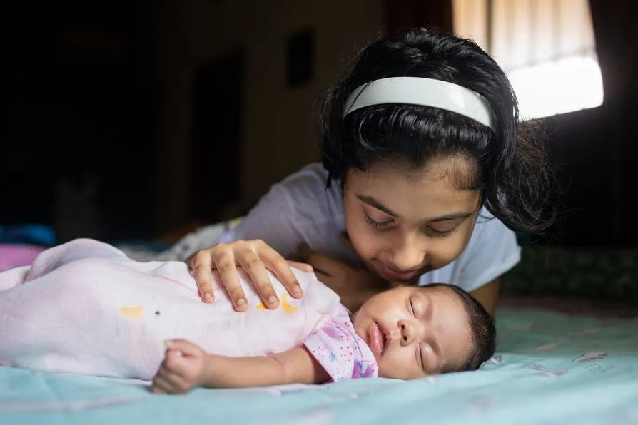 Girl cuddling newborn baby sibling